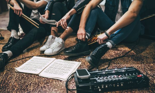 Repetition of rock music band. Cropped image of guitar players and drummer are sitting on the floor at rehearsal base with notes.